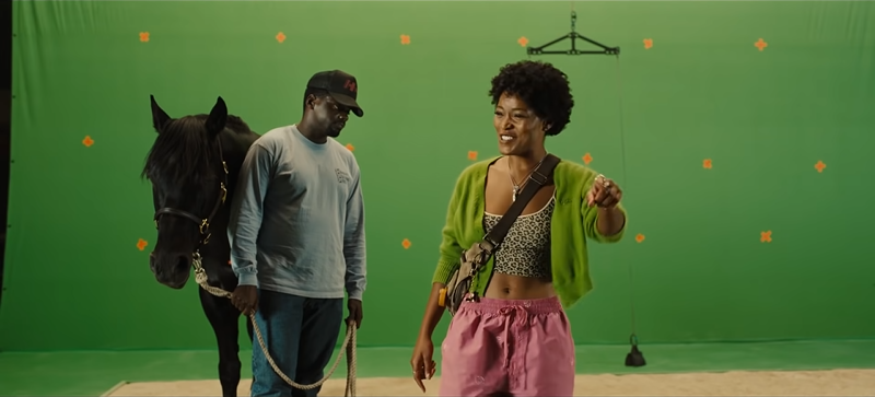 Keke’s character points into the film crew's camera.  Behind her is a green screen, while Daniel Kaluuya's character James stands with a black horse.